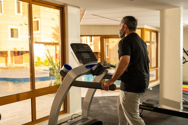Using sports equipment, practicing warm-up exercises, maintaining health and physical fitness, a young Arab Gulf Saudi man wearing sports clothes walking on the treadmill, sports club, engaging in enjoyable recreational activities.
