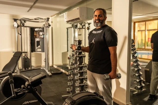 إيماءات القوة والعزم، الاهتمام بالصحة واللياقة الجسدية، رياضة كمال الأجسام، استخدام الاثقال الرياضية، رجل عربي خليجي سعودي يرتدي الزي الرياضي يقوم بممارسة تمارين رفع الأوزان، رجل سعودي يحمل بيده الأوزان، بناء الكتلة العضلية للجسم