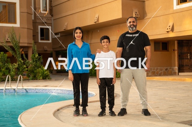 القيام بالأنشطة الترفيهية المسلية, مشاركة العائلة اللحظات الممتعة, قضاء العطلة الصيفية في المنتجعات السياحية, عائلة عربية خليجية سعودية تقف بجانب حوض السباحة في إحدى الفنادق بالسعودي، ممارسة رياضة السباحة الممتعة