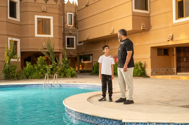 مشاركة العائلة اللحظات الممتعة, القيام بالأنشطة الترفيهية المسلية, قضاء العطلة الصيفية في المنتجعات السياحية, اب عربي خليجي سعودي يقف بجانب حوض السباحة مع ولده في إحدى الفنادق بالسعودي، ممارسة رياضة السباحة الممتعة
