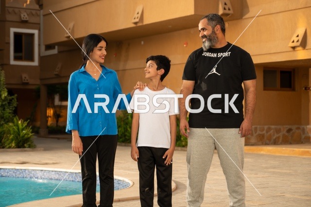القيام بالأنشطة الترفيهية المسلية, مشاركة العائلة اللحظات الممتعة, قضاء العطلة الصيفية في المنتجعات السياحية, عائلة عربية خليجية سعودية تقف بجانب حوض السباحة في إحدى الفنادق بالسعودي، ممارسة رياضة السباحة الممتعة