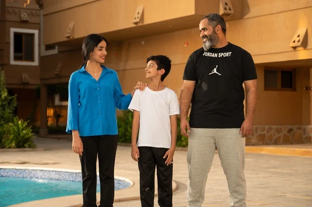 القيام بالأنشطة الترفيهية المسلية, مشاركة العائلة اللحظات الممتعة, قضاء العطلة الصيفية في المنتجعات السياحية, عائلة عربية خليجية سعودية تقف بجانب حوض السباحة في إحدى الفنادق بالسعودي، ممارسة رياضة السباحة الممتعة