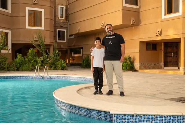 Spending the summer vacation in tourist resorts, sharing enjoyable moments with family, engaging in entertaining recreational activities, a Saudi Gulf Arab father standing by the swimming pool with his son in one of the hotels in Saudi Arabia, enjoying the fun sport of swimming.