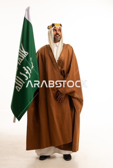 اليوم الوطني السعودي 23 سبتمبر، الفخر والاعتزاز بالهوية الوطنية، بورتريه لرجل عربي خليجي سعودي مبتسم يرتدي البشت وعقال التأسيس يحمل بيده علم تأسيس المملكة السعودية 22 فبراير، الاحتفال بيوم بدينا 1727 ، صورة الجسم بالكامل، خلفية بيضاء