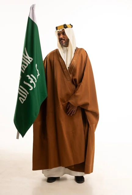 Saudi National Day is September 23, pride and honor in national identity, a portrait of a smiling Arab Gulf Saudi man wearing a bisht and the founding agal holding in his hand the flag of the establishment of the Saudi Kingdom on February 22, celebrating the Day of Our Beginning 1727, full-body image, white background.
