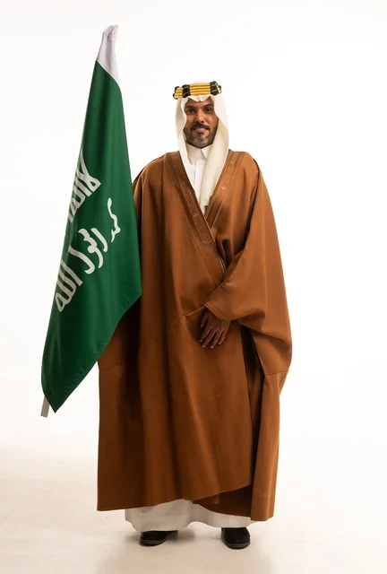 Saudi National Day is September 23, pride and honor in national identity, a portrait of a smiling Arab Gulf Saudi man wearing a bisht and the founding agal holding in his hand the flag of the establishment of the Saudi Kingdom on February 22, celebrating the Day of Our Beginning 1727, full-body image, white background.