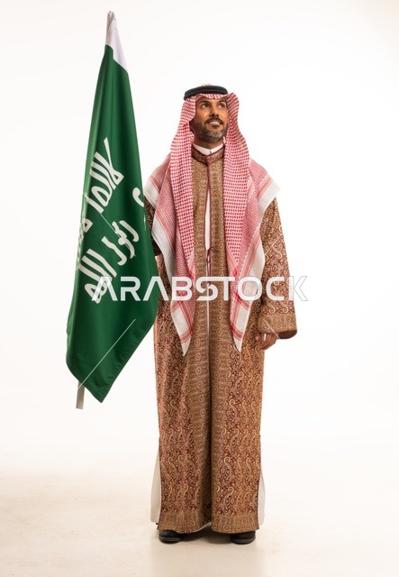 Wearing traditional attire on national occasions, Saudi National Day on September 23, pride and honor for the homeland, a portrait of a Saudi Arabian Gulf man wearing a ghutrah and thobe holding in his hand the flag of the establishment of the Kingdom of Saudi Arabia on February 22, celebrating the Day of Bidaya 1727, full-body image, white background.