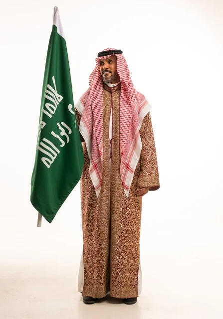 Wearing traditional attire on national occasions, Saudi National Day on September 23, pride and honor for the homeland, a portrait of a Saudi Arabian Gulf man wearing a ghutrah and thobe holding in his hand the flag of the establishment of the Kingdom of Saudi Arabia on February 22, celebrating the Day of Bidaya 1727, full-body image, white background.