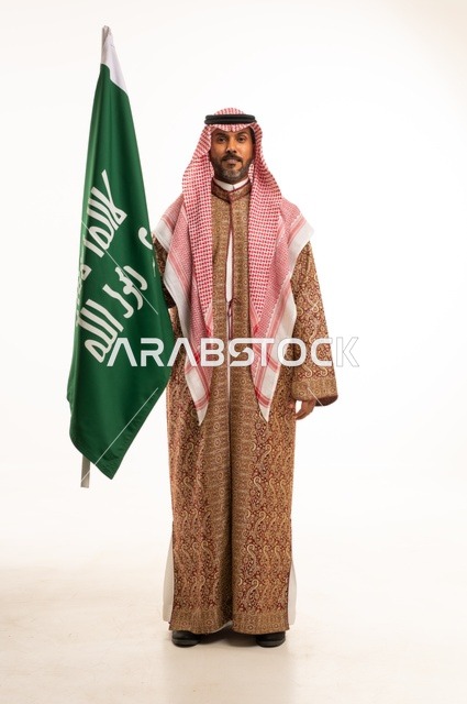 Wearing traditional attire on national occasions, Saudi National Day on September 23, pride and honor for the homeland, a portrait of a Saudi Arabian Gulf man wearing a ghutrah and thobe holding in his hand the flag of the establishment of the Kingdom of Saudi Arabia on February 22, celebrating the Day of Bidaya 1727, full-body image, white background.