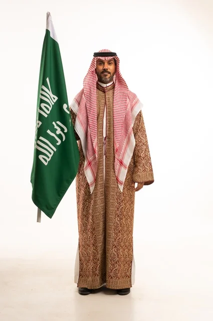 Wearing traditional attire on national occasions, Saudi National Day on September 23, pride and honor for the homeland, a portrait of a Saudi Arabian Gulf man wearing a ghutrah and thobe holding in his hand the flag of the establishment of the Kingdom of Saudi Arabia on February 22, celebrating the Day of Bidaya 1727, full-body image, white background.