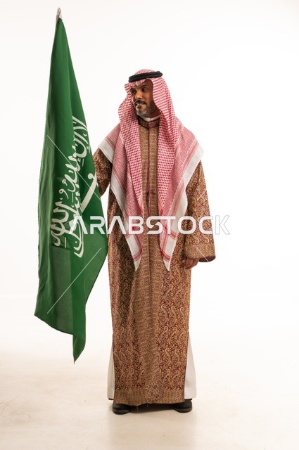 يوم العلم 11 مارس، ارتداء الازياء الشعبية في المناسبات الوطنية، اليوم الوطني السعودي 23 سبتمبر، الفخر والاعتزاز بالوطن، بورتريه لرجل عربي خليجي سعودي يرتدي الشماغ والدقلة يحمل بيده العلم السعودي، تأسيس المملكة السعودية 22 فبراير ، صورة الجسم بالكامل، خلفية بيضاء