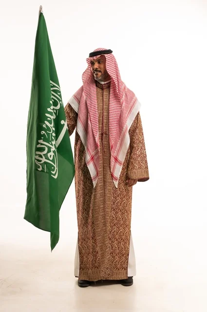 يوم العلم 11 مارس، ارتداء الازياء الشعبية في المناسبات الوطنية، اليوم الوطني السعودي 23 سبتمبر، الفخر والاعتزاز بالوطن، بورتريه لرجل عربي خليجي سعودي يرتدي الشماغ والدقلة يحمل بيده العلم السعودي، تأسيس المملكة السعودية 22 فبراير ، صورة الجسم بالكامل، خلفية بيضاء