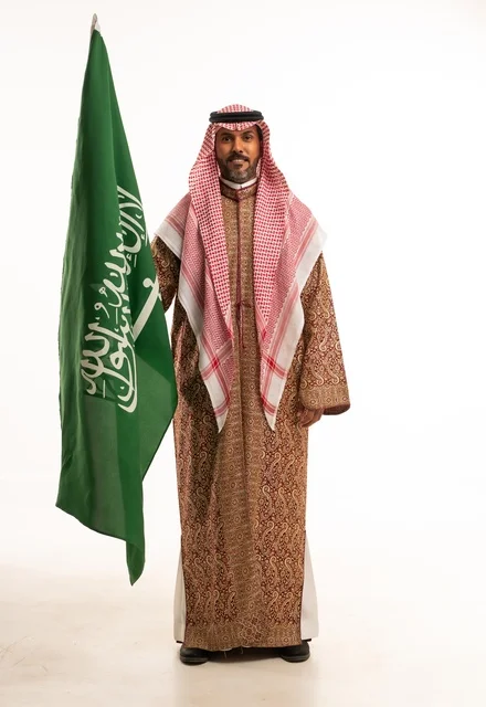 Flag Day is on March 11, wearing traditional clothing on national occasions, Saudi National Day is on September 23, pride and honor in the homeland, a portrait of an Arab Gulf Saudi man wearing a ghutrah and thobe holding the Saudi flag in his hand, the establishment of the Saudi Kingdom is on February 22, full-body image, white background.