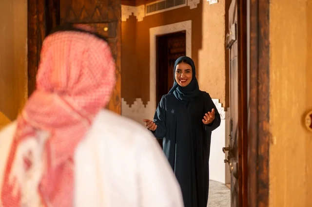 Greeting and reception at the door, the concept of love and understanding between spouses, a Saudi Arabian Gulf couple expressing gestures of longing and love joyfully welcoming the return of the absent, enjoyable moments and memories, spending quality family time, an entrance to a modern and decorated home.