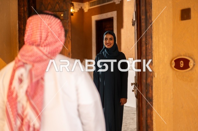 التحية والاستقبال عند الباب، مفهوم المحبة والتفاهم بين الزوجين، زوجان عربيان خليجيان سعوديان ايماءات الشوق والحب فرحا بعودة الغائب، لحظات وذكريات ممتعة، قضاء وقت عائلي ممتع، مدخل منزل عصري ومزخرف