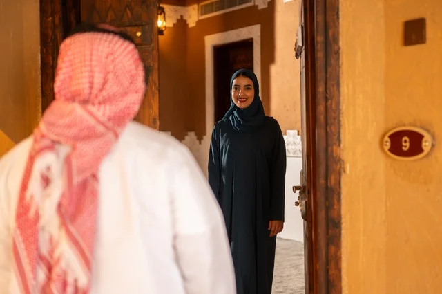 Greeting and reception at the door, the concept of love and understanding between spouses, a Saudi Arabian Gulf couple expressing gestures of longing and love joyfully welcoming the return of the absent, enjoyable moments and memories, spending quality family time, an entrance to a modern and decorated home.