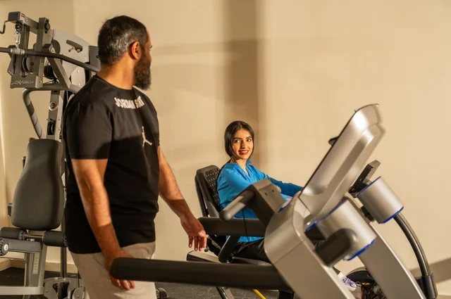 Exchanging entertaining conversations while exercising, maintaining fitness and physical agility, a Saudi Arabian man and woman wearing sports attire and engaging in morning exercise, a healthy lifestyle, spending enjoyable times with family outdoors.