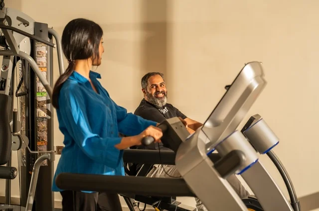 Exchanging entertaining conversations while exercising, maintaining fitness and physical agility, a Saudi Arabian man and woman wearing sports attire and engaging in morning exercise, a healthy lifestyle, spending enjoyable times with family outdoors.