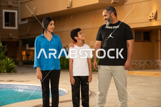 القيام بالأنشطة الترفيهية المسلية, مشاركة العائلة اللحظات الممتعة, قضاء العطلة الصيفية في المنتجعات السياحية, عائلة عربية خليجية سعودية تقف بجانب حوض السباحة في إحدى الفنادق بالسعودي، ممارسة رياضة السباحة الممتعة