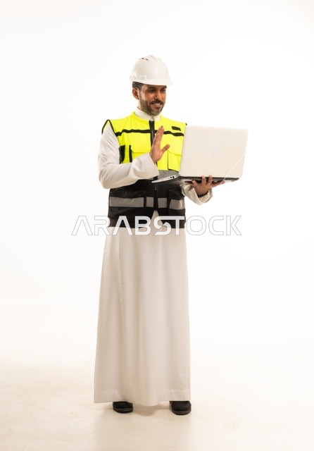 مفهوم ادارة المشاريع الهندسية والانشاءات، استخدام جهاز تقني حديث متطور في مجال الهندسة، العمل في القطاع الهندسي السعودي، مهنة ووظيفة شبابية، بورتريه لشاب مهندس عربي خليجي سعودي يرتدي الثوب التقليدي والسترة وخوذة الحماية يعمل على جهاز اللابتوب، خلفية بيضاء