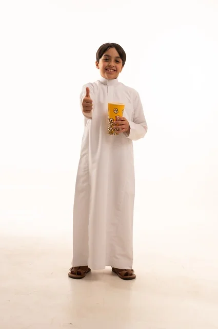 إشارة يد الأبهام للأعلى دليل علة الأعجاب، تناول الفوشار اللذيذ، بورتريه لفتى عربي خليجي سعودي يرتدي الزي التقليدي يحمل بيده علبة من الفشار الطازة ، الترفيه عن النفس وقضاء وقت ممتع، صورة الجسم بالطول الكامل، خلفية بيضاء