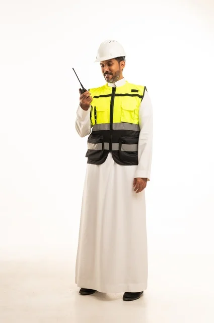 إعطاء أوامر خاصة بالعمل، مفهوم الهندسة و الإنشاءات المعمارية , استخدام جهاز الاتصال اللاسلكي في العمل , بورتريه لمهندس عربي خليجي سعودين يرتدي الثوب التقليدي مع السترة و خوذة الحماية , الجسم بالطول الكامل , خلفية بيضاء