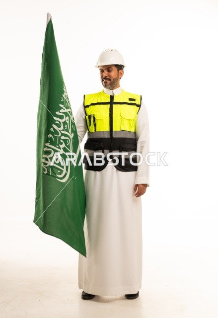 التطور العمراني بسواعد أبناء الوطن ، الاحتفال بيوم العلم 11 مارس، ذكرى اليوم الوطني السعودي 8 ربيع الاول، بورتريه لمهندس عربي خليجي سعودي مبتسم يرتدي سترة العمل وخوذة الحماية البيضاء في اليوم الوطني ويحمل علم المملكة، الجسم بالطول الكامل، خلفية بيضاء