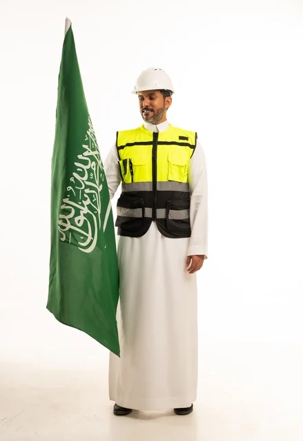 التطور العمراني بسواعد أبناء الوطن ، الاحتفال بيوم العلم 11 مارس، ذكرى اليوم الوطني السعودي 8 ربيع الاول، بورتريه لمهندس عربي خليجي سعودي مبتسم يرتدي سترة العمل وخوذة الحماية البيضاء في اليوم الوطني ويحمل علم المملكة، الجسم بالطول الكامل، خلفية بيضاء