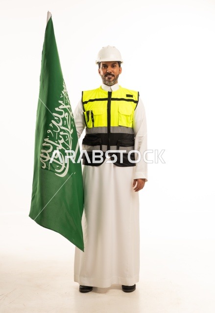 التطور العمراني بسواعد أبناء الوطن ، الاحتفال بيوم العلم 11 مارس، ذكرى اليوم الوطني السعودي 8 ربيع الاول، بورتريه لمهندس عربي خليجي سعودي مبتسم يرتدي سترة العمل وخوذة الحماية البيضاء في اليوم الوطني ويحمل علم المملكة، الجسم بالطول الكامل، خلفية بيضاء