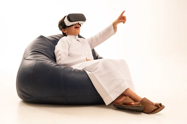 الإشارة باليد بأصبع السبابة لشئ ما يشاهده، بورتريه لطفل عربي خليجي سعودي سعيد يرتدي نظارة الواقع الإفتراضي ثلاثية الأبعاد الفريدة و العجيبة ،  التفاعل و المتعة و التسلية بمشاهدة الأفلام و ألعاب العالم الافتراضي ، تقنيات و ألعاب ، خلفية بيضاء