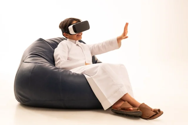 التفاعل و المتعة و التسلية بمشاهدة الأفلام و ألعاب العالم الافتراضي ، بورتريه لطفل عربي خليجي سعودي سعيد يرتدي نظارة الواقع الإفتراضي ثلاثية الأبعاد الفريدة و العجيبة ، الإشارة باليد بأصبع السبابة لشئ ما يشاهده، تقنيات و ألعاب ، خلفية بيضاء