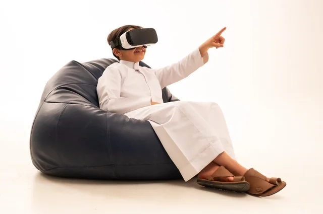 الإشارة باليد بأصبع السبابة لشئ ما يشاهده، بورتريه لطفل عربي خليجي سعودي سعيد يرتدي نظارة الواقع الإفتراضي ثلاثية الأبعاد الفريدة و العجيبة ،  التفاعل و المتعة و التسلية بمشاهدة الأفلام و ألعاب العالم الافتراضي ، تقنيات و ألعاب ، خلفية بيضاء