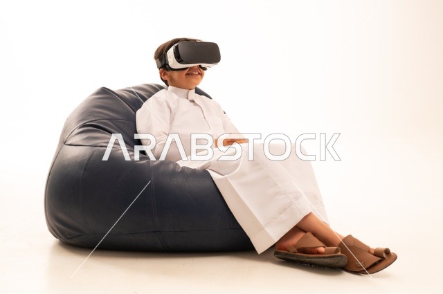 قضاء أوقات ممتعة ودمج التكنولوجيا في الحياة اليومية، التفاعل و المتعة و التسلية بمشاهدة الأفلام و ألعاب العالم الافتراضي ، بورتريه لطفل عربي خليجي سعودي سعيد يرتدي نظارة الواقع الإفتراضي ثلاثية الأبعاد الفريدة و العجيبة، تقنيات و ألعاب ، خلفية بيضاء
