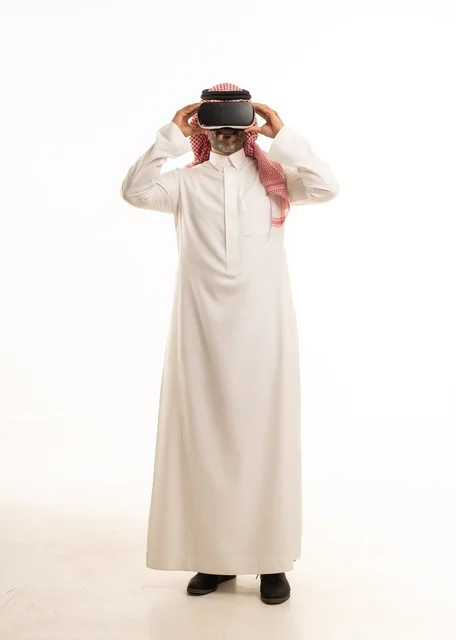 الاندماج والتفاعل مع العالم الخيالي، بورتريه لرجل عربي خليجي سعودي يرتدي الثوب والشماغ التقليدي ونظارات الواقع الافتراضي ثلاثية الأبعاد يحاول تجسيم شيء، دمج التقنيات والتكنولوجيا الحديثة مع المتعة والتسلية، الجسم بالطول الكامل، خلفية بيضاء