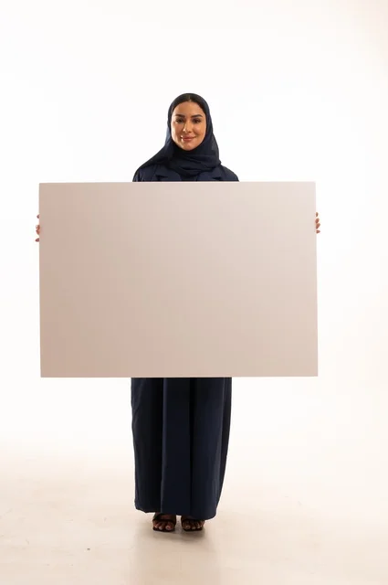 العروض والإعلانات التسويقية, بورتريه لإمرأة عربية خليجية سعودية ترتدي الحجاب والعباءة تمسك بيديها لوحة بيضاء مستطيلة فارغة، شابة سعودية تنظر إلى الكاميرا بتعابير الحزم والجدية، لوحات توضيحية ووسائل تعليمية, موك اب مستطيل أبيض, خلفية بيضاء