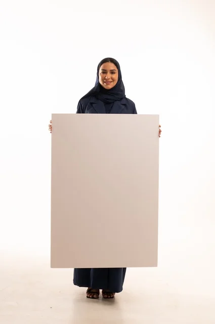 العروض والإعلانات التسويقية, بورتريه لإمرأة عربية خليجية سعودية ترتدي الحجاب والعباءة تمسك بيديها لوحة بيضاء مستطيلة فارغة، شابة سعودية تنظر إلى الكاميرا بتعابير الحزم والجدية، لوحات توضيحية ووسائل تعليمية, موك اب مستطيل أبيض, خلفية بيضاء