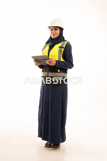 Standing with a straight back, women's professions and jobs in the engineering sector, the role of structural engineering in the development of Saudi society, a portrait of a Muslim Arab Gulf Saudi female engineer wearing a white helmet and safety vest working on a tablet, full-body, white background.