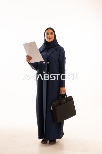 النظر بإيماءات التأمل والتمني، متابعة المهام اليومية المكتبية وقراءة الملاحظات, بورتريه لإمرأة عربية خليجية سعودية مبتسمه ترتدي العباءة تحمل حقيبة الأعمال وورقة بيضاء, أناقة النساء الخليجيات, الاهتمام بالمظهر الخارجي, الجسم بالطول الكامل، خلفية بيضاء
