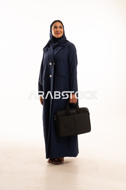 الوقوف باستقامة بإيماءات الجدية والثقة بالنفس, بورتريه لإمرأة عربية خليجية سعودية مبتسمه ترتدي العباءة تحمل حقيبة الأعمال, سيدة سعودية تنظر بايماءت السعاده و السرور, أناقة النساء الخليجيات, الاهتمام بالمظهر الخارجي, الجسم بالطول الكامل، خلفية بيضاء