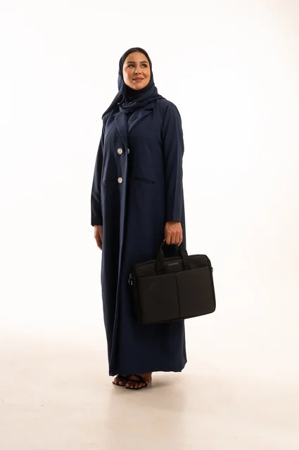الوقوف باستقامة بإيماءات الجدية والثقة بالنفس, بورتريه لإمرأة عربية خليجية سعودية مبتسمه ترتدي العباءة تحمل حقيبة الأعمال, سيدة سعودية تنظر بايماءت السعاده و السرور, أناقة النساء الخليجيات, الاهتمام بالمظهر الخارجي, الجسم بالطول الكامل، خلفية بيضاء