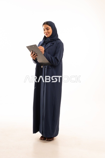 كتابة وتدوبن الملاحظات على لوح كليب بورد, بورتريه لإمرأة عربية خليجية سعودية مبتسمه ترتدي العباءة, سيدة سعودية تنظر بايماءت السعاده و السرور, أناقة النساء الخليجيات, الاهتمام بالمظهر الخارجي, الجسم بالطول الكامل، خلفية بيضاء