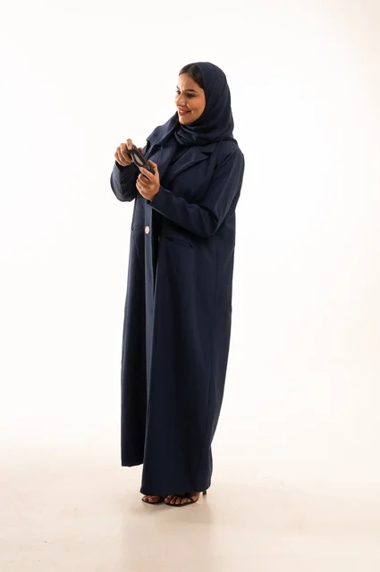 مفهوم الاندماج والتفاعل باللعب ألعاب البلايستيشن، قضاء أوقات ممتعة, بورتريه لشابة عربية خليجية سعودية ترتدي العباءة، سيده سعوديه تمسك بيدها عصا التحكم عن بعد تلعب بألعاب الفيديو، التقنيات الالكترونية الحديثة، الجسم بالطول الكامل، خلفية بيضاء