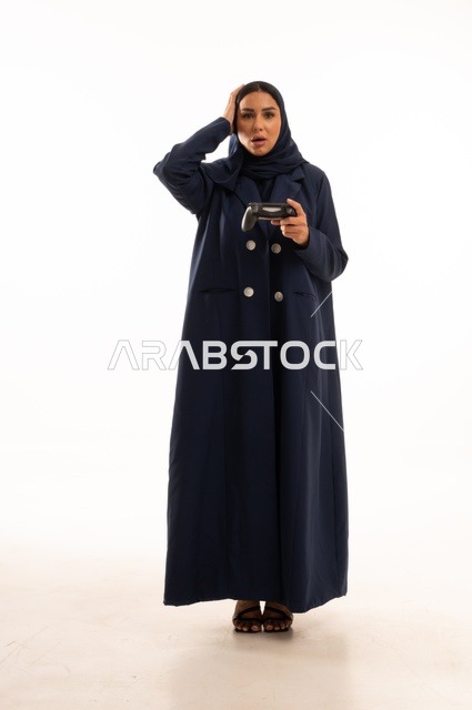 تعابير وجه ويد تدل على الخسارة والحزن، مفهوم الاندماج والتفاعل باللعب ألعاب البلايستيشن، قضاء أوقات ممتعة, بورتريه لشابة عربية خليجية سعودية ترتدي العباءة، سيده سعوديه تمسك بيدها عصا التحكم عن بعد تلعب بألعاب الفيديو، الجسم بالطول الكامل، خلفية بيضاء