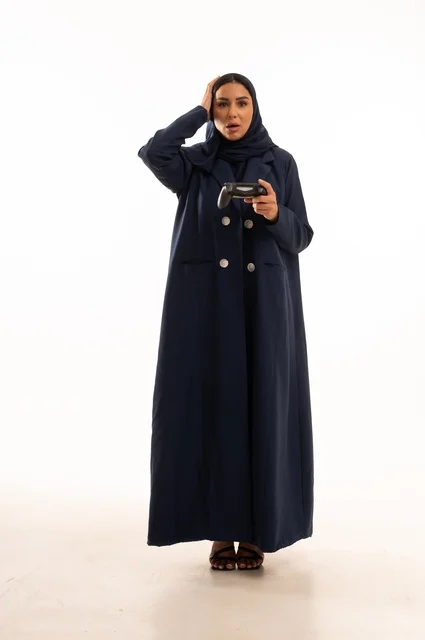 Facial and hand expressions indicating loss and sadness, the concept of integration and interaction while playing PlayStation games, spending enjoyable times, a portrait of a young Arab Gulf Saudi woman wearing an abaya, a Saudi woman holding a remote control playing video games, full-body, white background.
