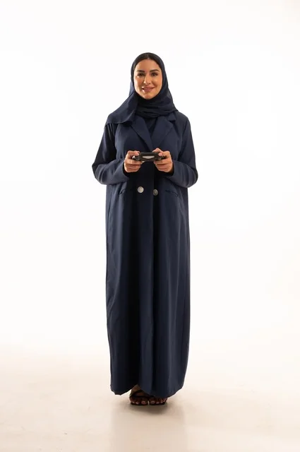 الألعاب الالكترونية والأجهزة الحديثة، مفهوم الاندماج والتفاعل باللعب ألعاب البلايستيشن، قضاء أوقات ممتعة, بورتريه لشابة عربية خليجية سعودية ترتدي العباءة، سيده سعوديه تمسك بيدها عصا التحكم عن بعد تلعب بألعاب الفيديو، الجسم بالطول الكامل، خلفية بيضاء