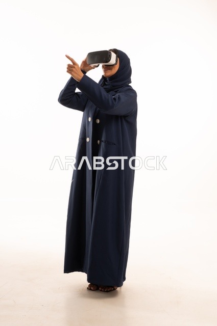 الإشارة باليد بأصبع السبابة لشئ ما يشاهده، بورتريه لإإمرأة عربية خليجية سعودية سعيدة ترتدي نظارة الواقع الإفتراضي ثلاثية الأبعاد الفريدة و العجيبة، التفاعل و المتعة و التسلية بمشاهدة الأفلام و ألعاب العالم الافتراضي ، تقنيات و ألعاب ، خلفية بيضاء