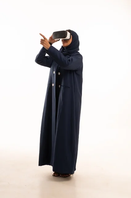الإشارة باليد بأصبع السبابة لشئ ما يشاهده، بورتريه لإإمرأة عربية خليجية سعودية سعيدة ترتدي نظارة الواقع الإفتراضي ثلاثية الأبعاد الفريدة و العجيبة، التفاعل و المتعة و التسلية بمشاهدة الأفلام و ألعاب العالم الافتراضي ، تقنيات و ألعاب ، خلفية بيضاء