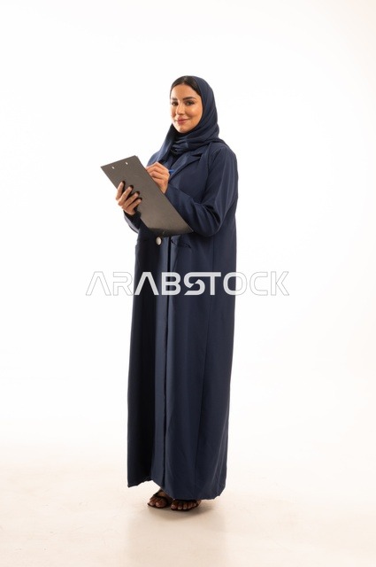 كتابة وتدوبن الملاحظات على لوح كليب بورد, بورتريه لإمرأة عربية خليجية سعودية مبتسمه ترتدي العباءة, سيدة سعودية تنظر بايماءت السعاده و السرور, أناقة النساء الخليجيات, الاهتمام بالمظهر الخارجي, الجسم بالطول الكامل، خلفية بيضاء