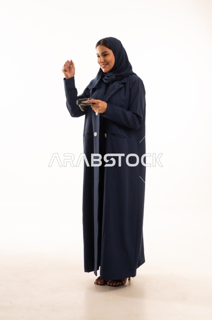 قضاء أوقات ممتعة, بورتريه لشابة عربية خليجية سعودية ترتدي العباءة، سيده سعوديه تمسك بيدها عصا التحكم عن بعد تلعب بألعاب الفيديو بإيماءات وجه ويدين مختلفة تدل على الفوز والإنتصار، الجسم بالطول الكامل، خلفية بيضاء