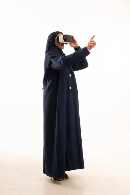 الإشارة باليد بأصبع السبابة لشئ ما يشاهده، بورتريه لإإمرأة عربية خليجية سعودية سعيدة ترتدي نظارة الواقع الإفتراضي ثلاثية الأبعاد الفريدة و العجيبة، التفاعل و المتعة و التسلية بمشاهدة الأفلام و ألعاب العالم الافتراضي ، تقنيات و ألعاب ، خلفية بيضاء